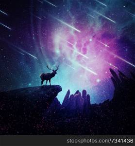 Majestic deer with long stand on the peak of a rocky hill below a wonderful night sky with falling stars and sparkles. Mystic wild scene screen saver.