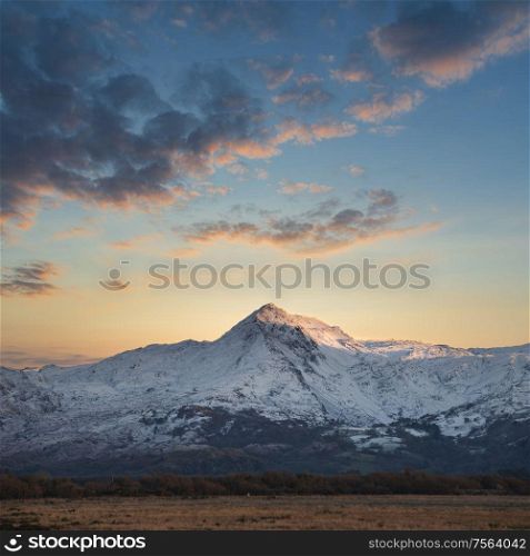 Majestic landscape image of Snowdonia snowcapped mountains with dramatic sunset clouds and beautiful vibrant glow