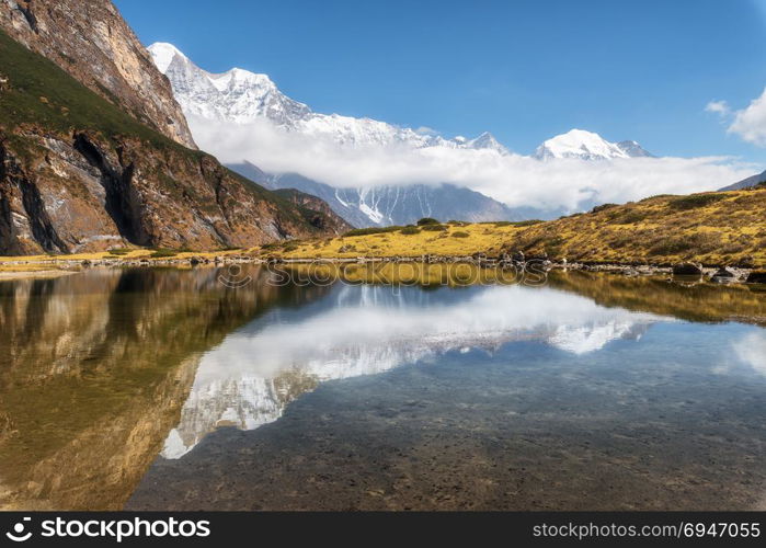 Majestic mountains with high rocks with snow covered peaks, mountain lake, beautiful reflection in water, blue sky with clouds in sunset. Nepal. Amazing tranquil landscape with mountains. Himalayas. Majestic mountains with beautiful reflection in water