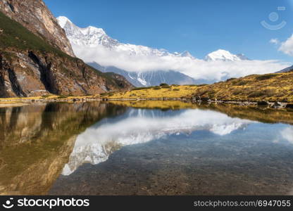 Majestic mountains with high rocks with snow covered peaks, mountain lake, beautiful reflection in water, blue sky with clouds in sunset. Nepal. Amazing tranquil landscape with mountains. Himalayas. Majestic mountains with beautiful reflection in water