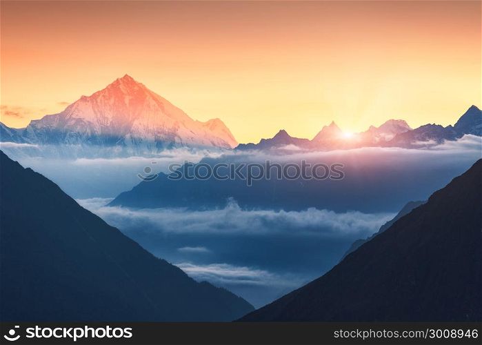 Majestic scene of silhouettes of mountains and low clouds at colorful sunrise in Nepal. Landscape with snowy peaks of mountains, beautiful sky and yellow sunlight. Rocks and sun rays.Nature background