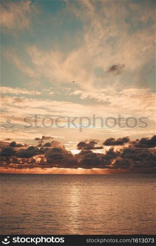 Majestic sun flares coming through the clouds during a sunset over the ocean on orange tones and with copy space
