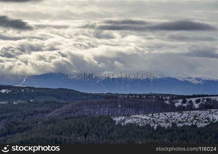 Majestic view of cloudy sky, winter mountain, snowy glade, conifer and deciduous forest from Plana mountain toward Rila mountain, Bulgaria, Europe