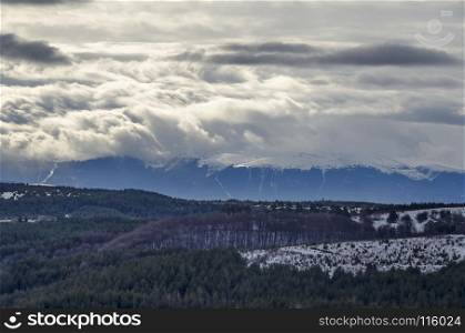 Majestic view of cloudy sky, winter mountain, snowy glade, conifer and deciduous forest from Plana mountain toward Rila mountain, Bulgaria, Europe