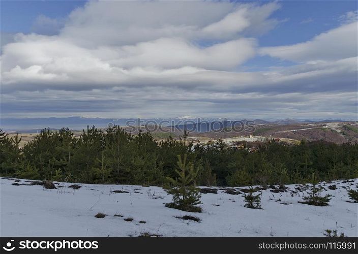 Majestic view of cloudy sky, winter mountain, snowy glade, residential district, conifer and deciduous forest from Plana mountain toward Balkan mountain or Stara planina, Bulgaria, Europe