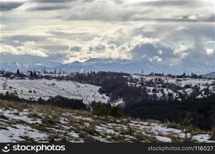Majestic view of cloudy sky, winter mountain, snowy glade, residential district, conifer and deciduous forest from Plana mountain toward Rila mountain, Bulgaria, Europe