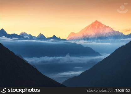 Majestic view of silhouettes of mountains and low clouds at colorful sunrise in Nepal. Landscape with snowy peaks of Himalayan mountains, beautiful sky and yellow sun rays. Amazing Himalayas. Nature