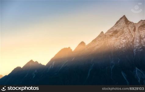 Majestic view of silhouettes of mountains and low clouds at colorful sunrise in Nepal. Landscape with snowy peaks of Himalayan mountains, beautiful sky and yellow sun rays. Amazing Himalayas. Nature