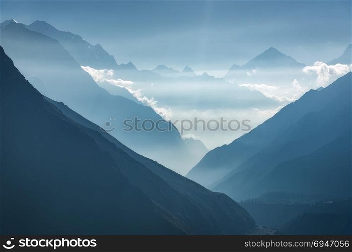Majestic view of silhouettes of mountains and low clouds at sunset in Nepal. Landscape with high rocks of Himalayan mountains, beautiful blue sky and sun rays. Amazing Himalayas. Nature background . Majestic view of silhouettes of mountains and low clouds at sunset