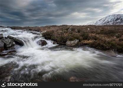 Majestic Winter landscape image of River Etive in foreground with iconic snowcapped Stob Dearg Buachaille Etive Mor mountain in the background