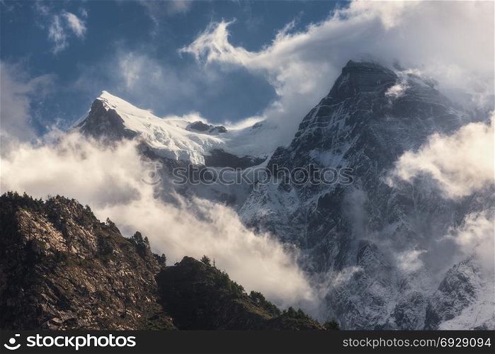 Majestical scene with mountains with snowy peaks in clouds in Nepal. Colorful landscape with beautiful high rocks and dramatic cloudy sky at sunset. Nature background. Fairy scene. Amazing mountains