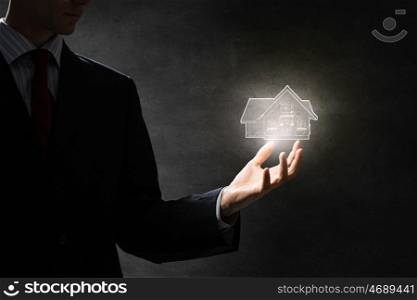 Make investment in construction. Hand of businessman holding glowing house model on dark background