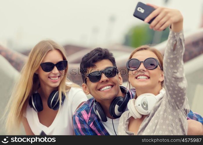 Make selfie photos with friends. Three young happy people sitting outdoors and making selfie