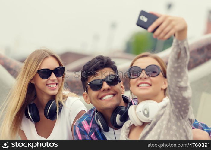 Make selfie photos with friends. Three young happy people sitting outdoors and making selfie