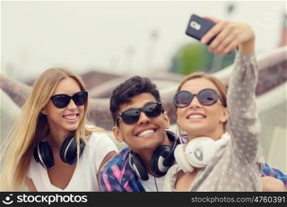 Make selfie photos with friends. Three young happy people sitting outdoors and making selfie