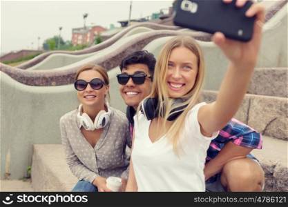 Make selfie photos with friends. Three young happy people sitting outdoors and making selfie