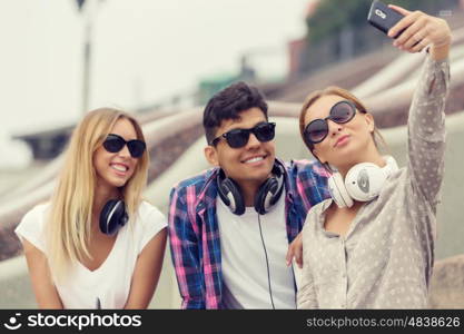 Make selfie photos with friends. Three young happy people sitting outdoors and making selfie