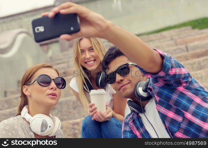 Make selfie photos with friends. Three young happy people sitting outdoors and making selfie