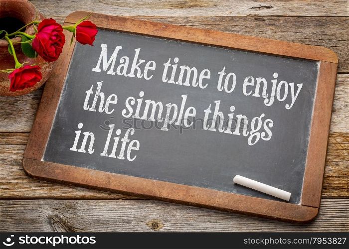 Make time to enjoy the simple things inspirational advice - white chalk text on a vintage slate blackboard with red roses against rustic wood