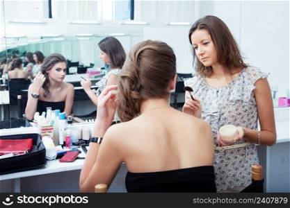 Make-up artist and model at work in front of mirror, selective focus on MUA looking at model
