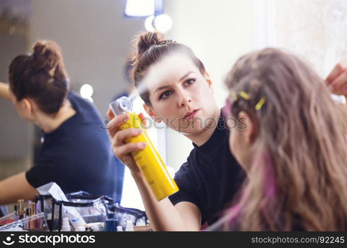 Make-up artist applying hairspray on model's hair, focus on make-up artist