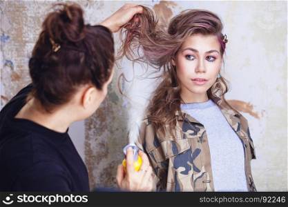 Make-up artist applying hairspray on model's hair, focus on model
