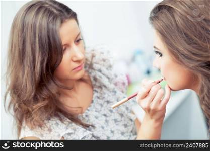 Make-up artist applying lip liner on model’s lips, close-up, selective focus on model