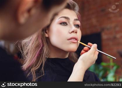 Make-up artist applying lipstick with a brush on model's lips, close up on model's face