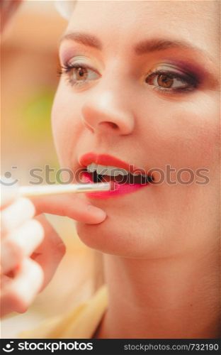 Make up artist applying lipstick with brush on pretty gorgeous woman lips. Closeup of visagiste and young girl. Beauty and makeup concept.. Make up artist applying lipstick with brush.