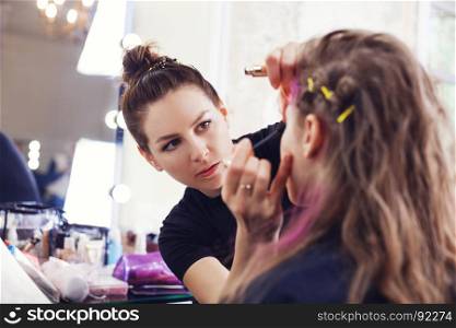 Make-up artist applying mascara on model's eyelashes, selective focus on make up artist