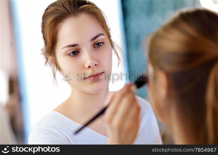 Make-up artist applying powder with a brush on model&rsquo;s cheeks, selective focus on MUA
