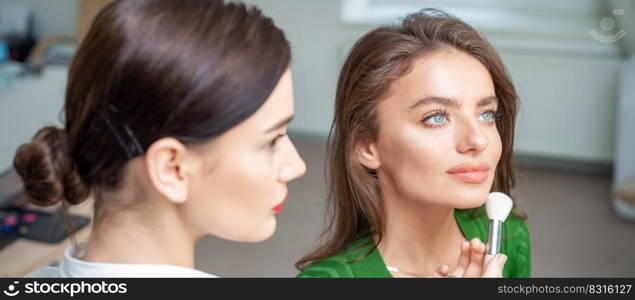 Make up artist applying professional make up of tonal foundation on the face of beautiful young caucasian woman in make up room. Base for make up.. Make up artist applying professional make up of tonal foundation