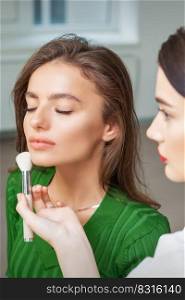 Make up artist applying professional make up of tonal foundation on the face of beautiful young caucasian woman in make up room. Base for make up.. Make up artist applying professional make up of tonal foundation