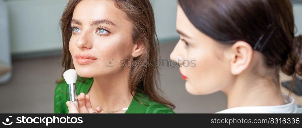 Make up artist applying professional make up of tonal foundation on the face of beautiful young caucasian woman in make up room. Base for make up.. Make up artist applying professional make up of tonal foundation