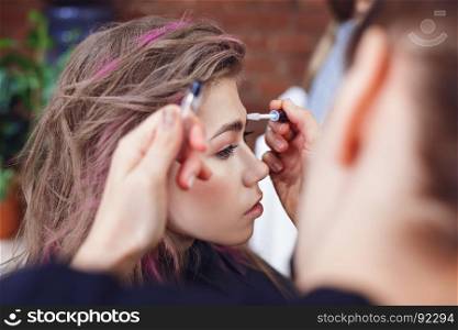 Make-up artist fixing model's eyebrows with gel, selective focus on model's eyes