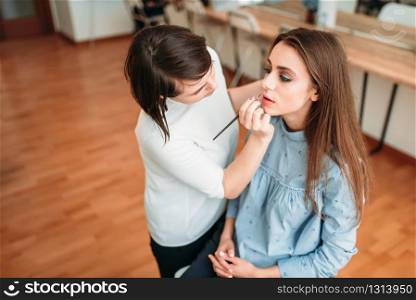 Make up artist hand with brush applying gloss on woman lips. Professional female beautician work with glamour attractive girl. Make up artist hand applying gloss on woman lips