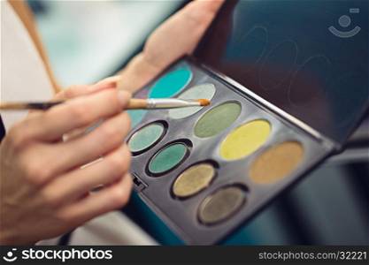 Make-up artist holding a palette of colorful eyeshadows and a brush, close up