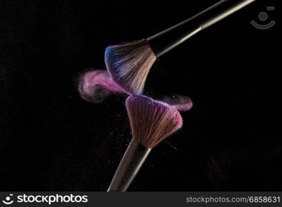 Make-up brushes with pink powder explosion on black background