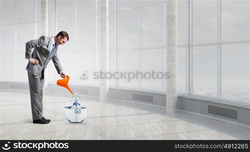 Make your income grow. Businessman in office pouring water from can to fishbowl