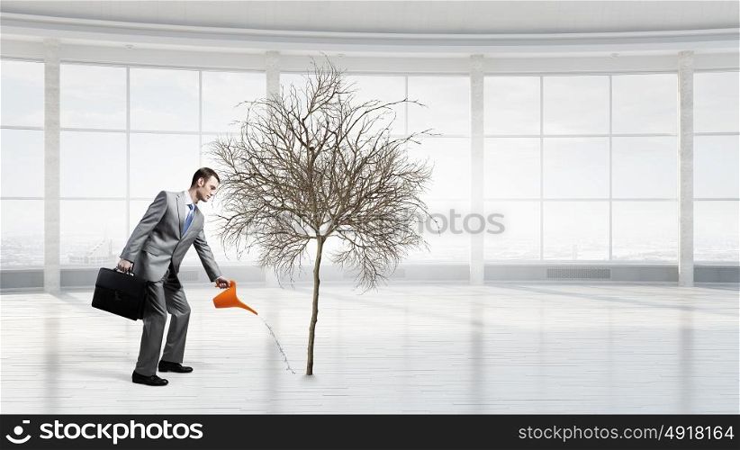 Make your income grow. Young cheerful businessman watering dry tree with can