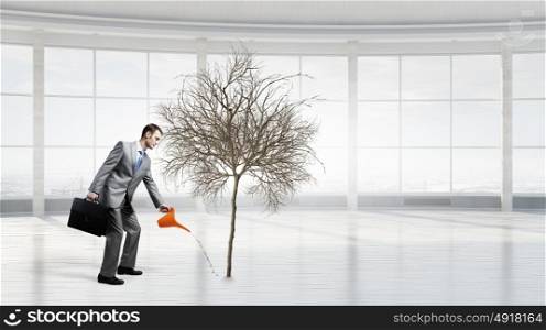 Make your income grow. Young cheerful businessman watering dry tree with can