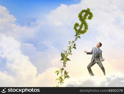 Make your income grow. Young cheerful businessman watering green dollar sprout with can