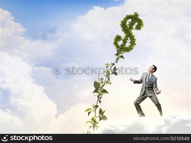 Make your income grow. Young cheerful businessman watering green dollar sprout with can