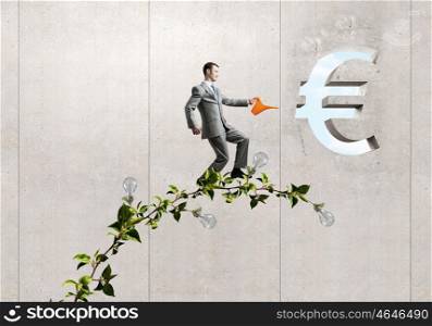 Make your income grow. Young cheerful businessman watering green euro sprout with can