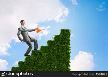 Make your income grow. Young cheerful businessman watering green growing graph with can