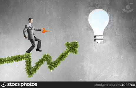 Make your income grow. Young cheerful businessman watering green growing graph with can