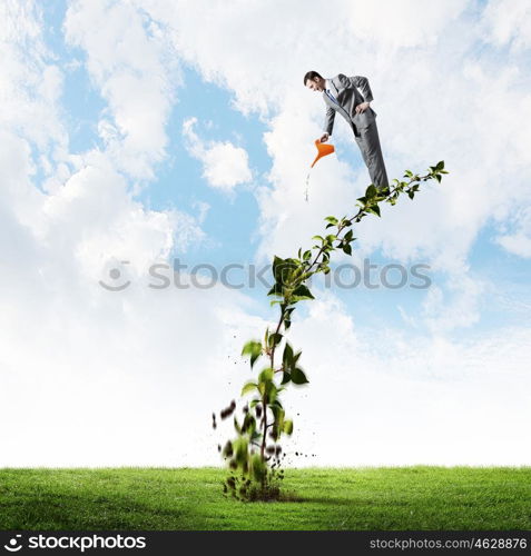 Make your income grow. Young cheerful businessman watering green sprout with can