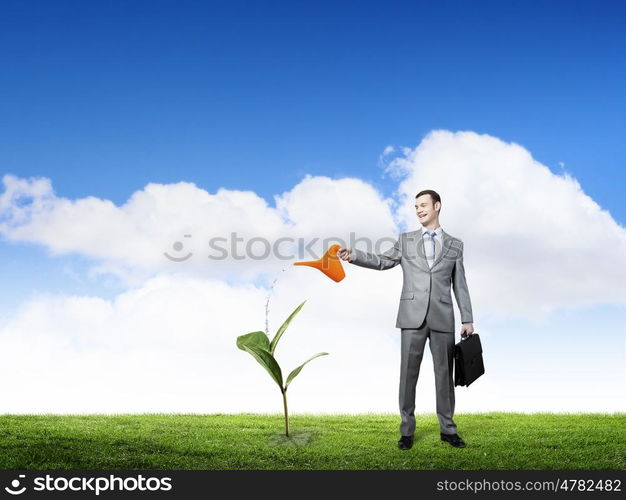 Make your income grow. Young cheerful businessman watering green sprout with can