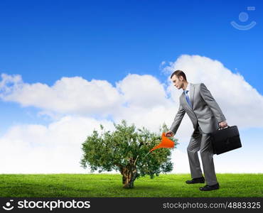 Make your income grow. Young cheerful businessman watering green sprout with can