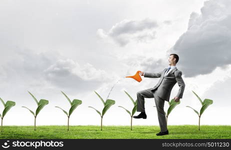 Make your income grow. Young cheerful businessman watering green sprout with can